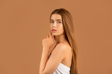Millennial woman with long straight hair touching her face, having soft healthy skin and nude...
