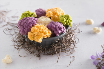 Coliflor de colores, verde, naranja, morado y blanco en un recipiente gris sobre mesa blanca