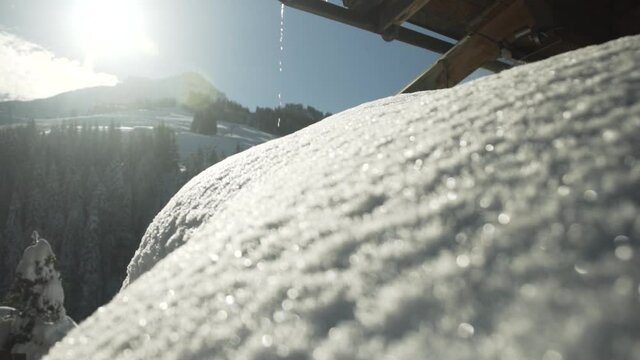 Focus pull from mountain with snowy trees in the background to snow on a roof with water dripping