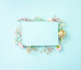 Bright Easter spring creative layout. Flowers of gypsophila and carnations of white and pastel pink colors with gold  egg on a light blue background with copy space. Flat lay. Top view. - obrazy, fototapety, plakaty