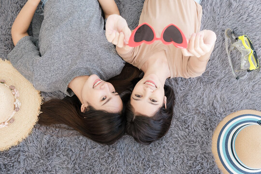 Portrait of two young Asian women show sunglasses in summer concept smiling and lying on the white floor to selfy take a photo. - Powered by Adobe