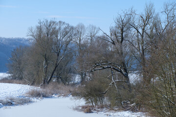 Eine winterliche Landschaft an einem Gewässer bei Schnee und Eis unter schönen blauen Himmel mit...