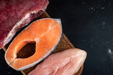 Fresh raw meat, salmon and chicken fillet on wooden cutting board on black background. Natural food...