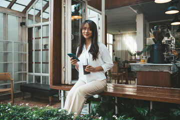 Cute asian young woman sitting in cafe with coffee and phone