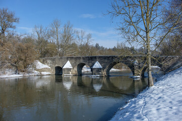 Fototapeta na wymiar Mittelalterliche Steinbrücke an der Altmühl im Winter bei Schnee und blauem Himmel