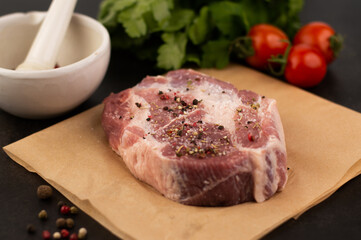 Blurred image of a piece of seasoned raw pork, condiments, mortar, herbs, tomatoes.