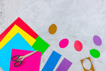 scissors, colored paper, and cut-out eggs on a concrete background