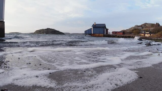 Waves breaking against the beach one cloudy evening in autumn in Gothenburg, Sweden. Bath cabins and island in background. 4K footage, slow motion x2