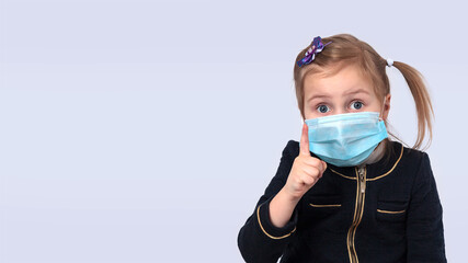 Child in a medical mask pointing up with his forefinger.