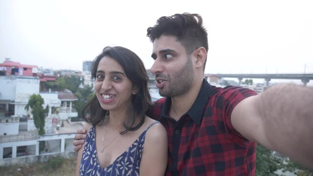 Happy and beautiful couple taking funny selfie portrait while standing on rooftop.Asian man and woman taking selfie and having fun together while making funny faces.Funny couple making selfie video