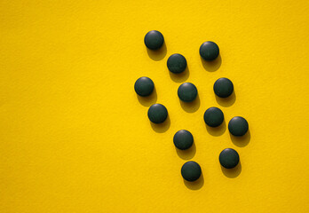 Organic spirulina tablets on the yellow background. Group of dark pads. View from top.