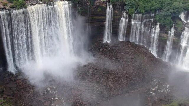 From the center of Calandula waterfalls in Angola panning down to where the water hitting the black rocks and the mist all around the waterfall Aerial
