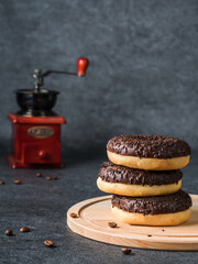 Chocolate donuts with coffee, lying on top of each other on a wooden board. Dark background