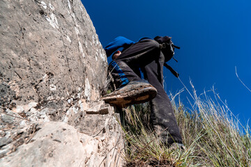 Faceless person wearing sportswear climbing the mountain during sunny day.