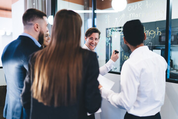 Group of positive colleagues standing near glass with business scheme