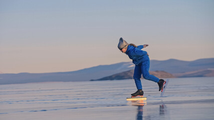 The girl train on ice speed skating. The child skates in the winter in blue sportswear suit, sport glasses. Children speed skating sport. Outdoor slow motion. Snow capped mountains, beautiful ice.