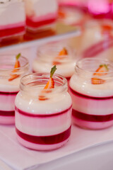 Wedding candy bar, single serving desserts of white and red color in small jars made of glass on a white table