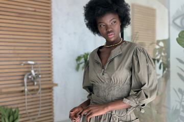 portrait photo of a beautiful dark-skinned girl with afro hair in green dress who stands in studio, looks away and posing