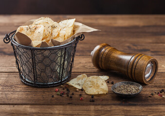 Crunchy potato crisps chips with  black pepper in steel snack bucket on wooden background with mill...