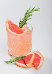 Red grapefruit cocktail with fruit slice and rosemary on white background.