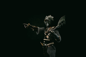 Medieval fighter in armor, pointing a finger at a direction, in profile, an ax on his shoulder - obrazy, fototapety, plakaty