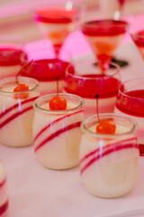 Wedding candy bar, single serving desserts of white and red color in small jars made of glass on a white table