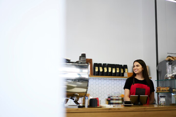 Cheerful brunette female barista standing at bar at coffee shop working space enjoying retailing...