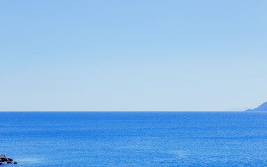 Seascape with light blue skies, blue sea, cliff islands and a distant horizon.