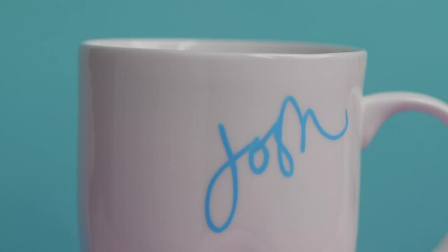 closeup woman writing Josh in cursive on white coffee mug with light blue freely marker