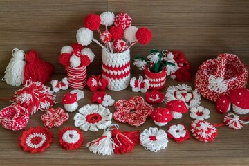 Obraz premium Set of white and red crochet yarn figures: flowers pompoms butterflies vase basket, as martenitsa, bulgarian folklore tradition in March Baba Marta day. Shallow depth, brown wooden texture background.