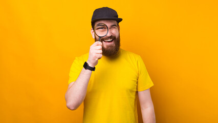 Cheerful young man with beard looking trough magnifying glass.