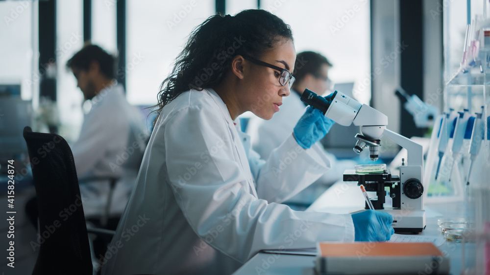 Wall mural medical science laboratory: beautiful black scientist looking under microscope does analysis of test