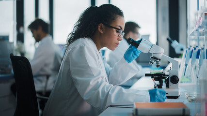 Medical Science Laboratory: Beautiful Black Scientist Looking Under Microscope Does Analysis of...