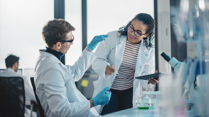 Obraz premium Modern Medical Research Laboratory: Portrait of Two Young Scientists Mixing Liquid Chemicals, Checking Result. Digital Tablet, Talking. Diverse Team of Multi-Ethnic Specialists work in Advanced Lab