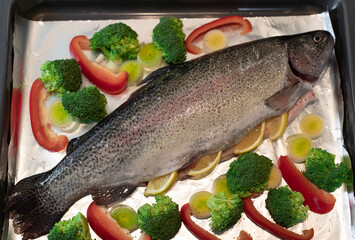whole raw rainbow trout with broccoli, leek, red pepper and spices on baking tray. Ready for baking. close-up