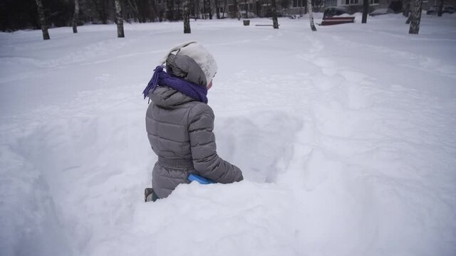The girl is digging the snow. The child plays with a lot of snow. A rosy child in the cold. Nice walk and play