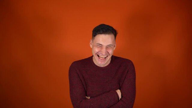 Portrait of laughing man on orange background. Happy whinny guy expresses positive emotions, looking at camera.
