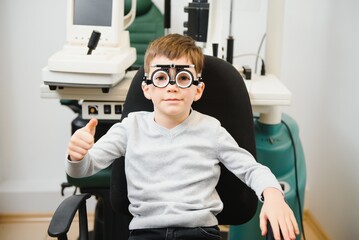 Fototapeta na wymiar Small serious boy sitting on chair office of vision test. doctor picks up lenses to special glasses