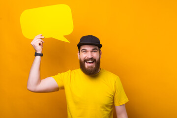 Happy smiling man with beard in yellow shirt holding empty blank speech bubble.