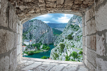View from stone window of Cetina River, mountains and old town Omis, Croatia. View from above of Cetina river canyon and mouth in Omis, Dalmatia region of Croatia