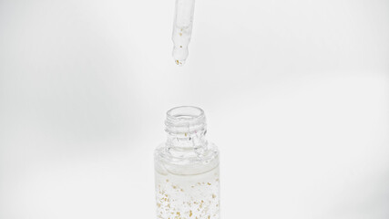 close up of pipette above glass bottle with essential oil on white