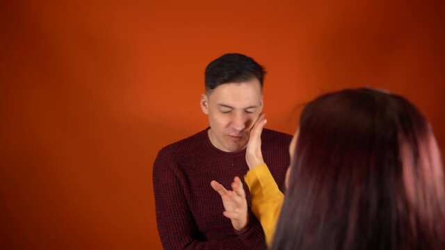 Crop person slapping scared man in face. Emotional male getting slapped in face while shouting with closed eyes in fear on orange background.