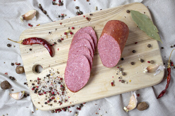 Appetizing sausage sliced on a wooden cutting board on a rough linen background with spices, close up top view