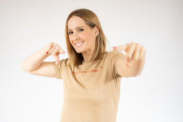 Photo of happy young woman in casual t-shirt standing isolated over white background. Looking camera while pointing to you.