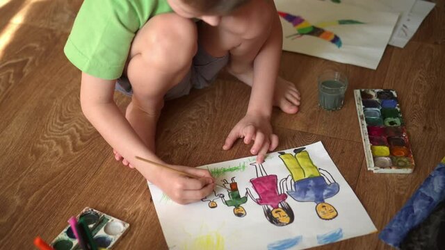 A child paints a drawing on the floor with watercolors. Drawing depicting a family.