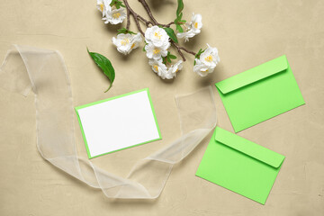 Spring invitation blank card mockup, ribbon, envelopes and decorative blooming sakura branch. Beige concrete background. Stationery scene. Top view, flat lay.