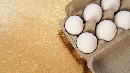 White chicken eggs in a cardboard tray on a gold background. Background with place for text. Healthy food and Easter concept. Protein food