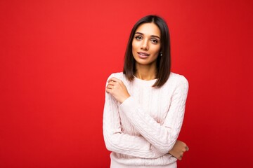 Fototapeta premium Portrait of positive cheerful cute smiling young brunette woman in casual sweater isolated on red background with copy space