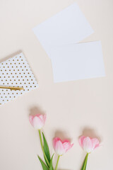 Work space concept with clipboard, notebook, pen, pink tulip flowers and accessories on beige background. Flat lay and top view