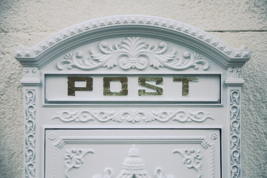 The elegant white slot of a luxury mailbox, with the word Post. Isolated on a creamy white wall surface.
